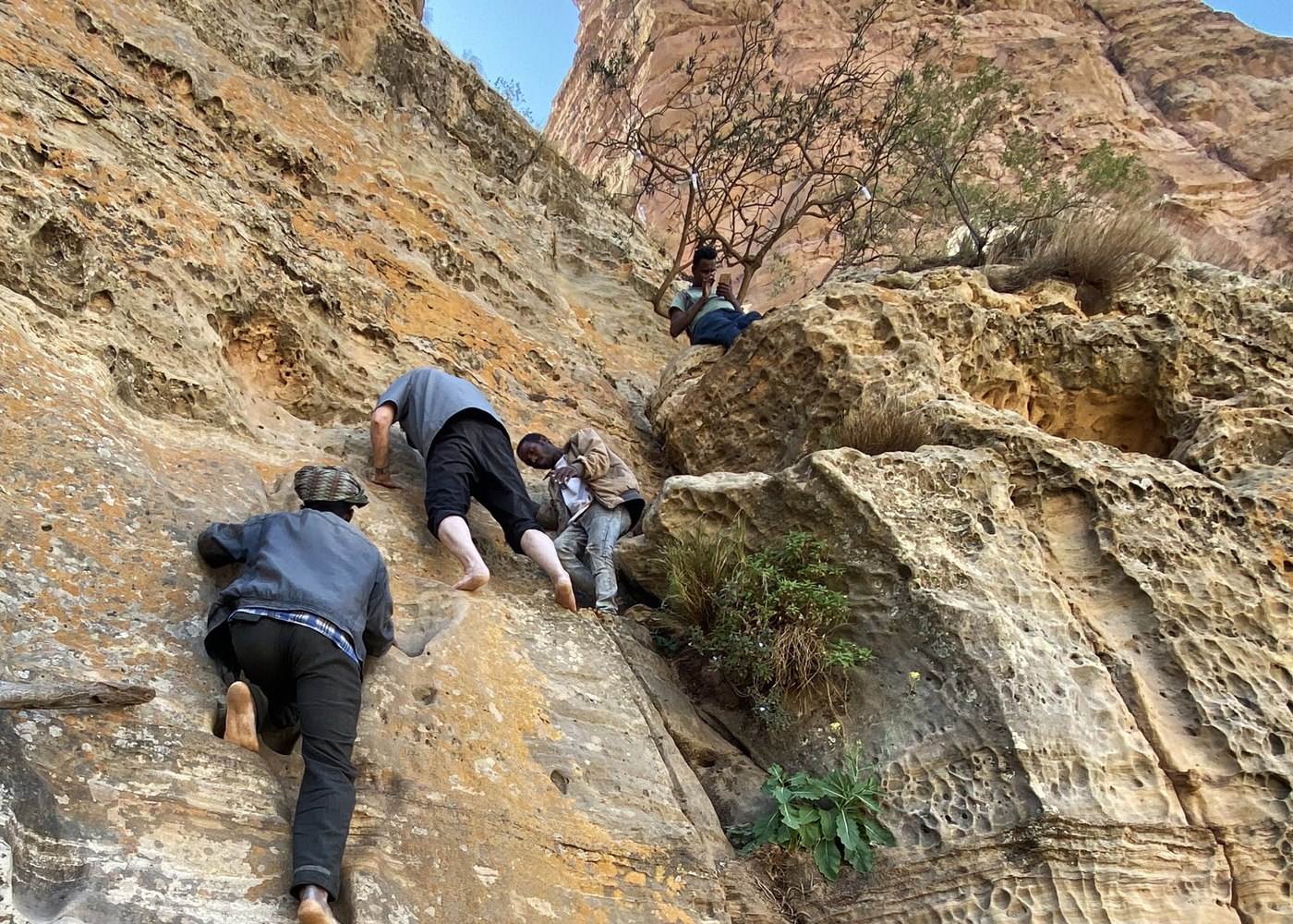 Visitors climb the exposed sandstone approach to Abuna Yemata Guh with local guides in Tigray, Ethiopia.